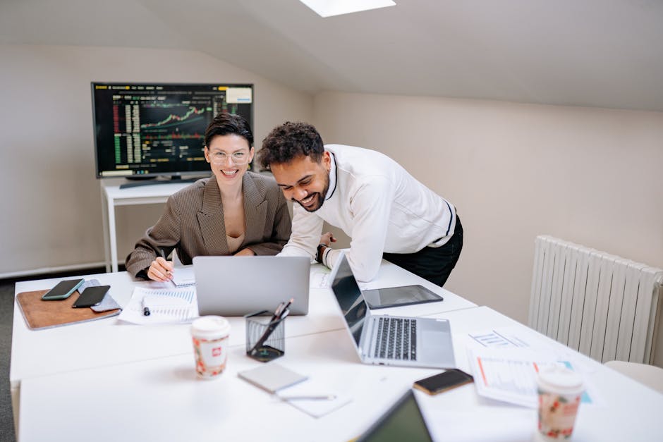 Two colleagues engaging in teamwork with laptops and documents, smiling in a modern office.